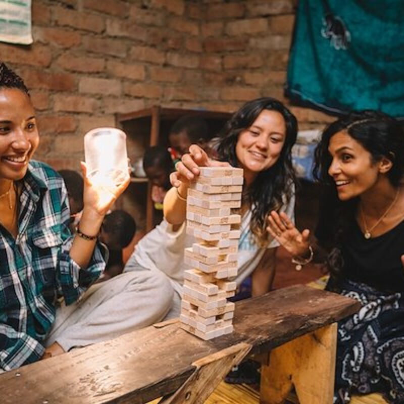 a large family sits on the ground around a low table and plays Jenga in a house that just received electricity and lights