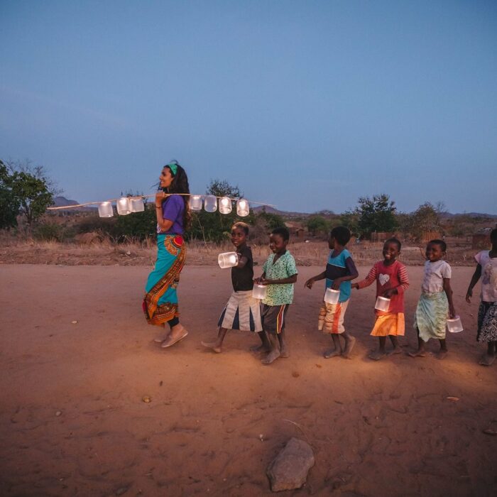 a line of children follows a young woman across the desert with newly received lights and lanterns