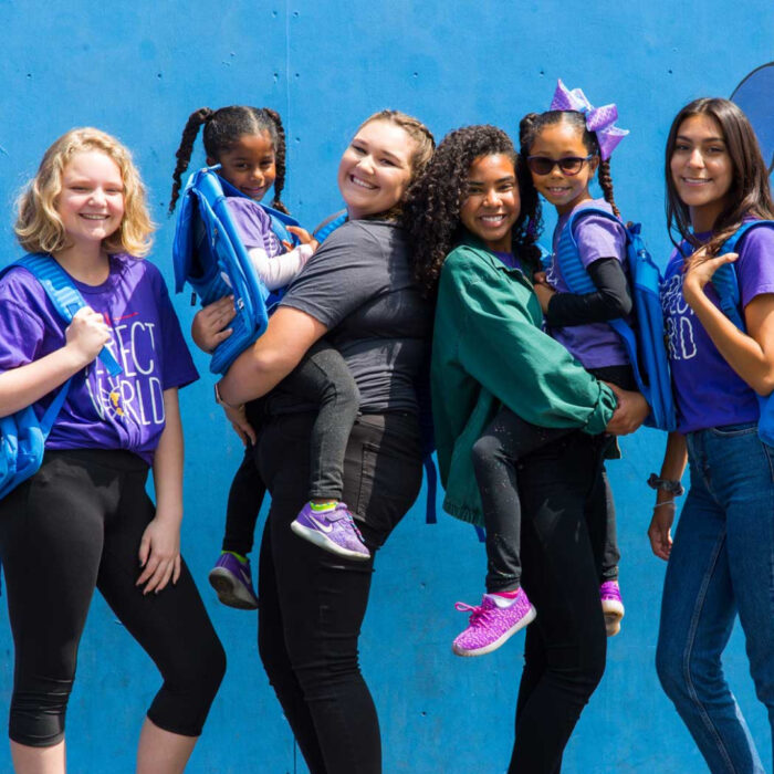 a group of diverse school kids of different ages pose for the camera on a blue background