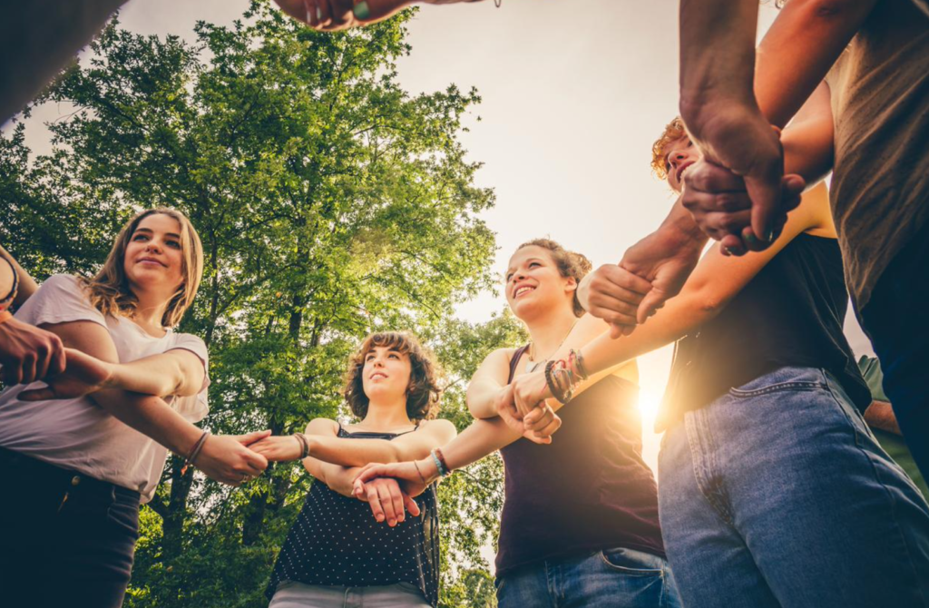 Group of diverse youth leaders forming a circle and showing unity by holding each others' hands.