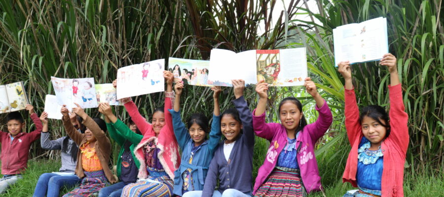 a group of students wearing bright clothing in Guatemala hold up signs and artwork they made above their heads