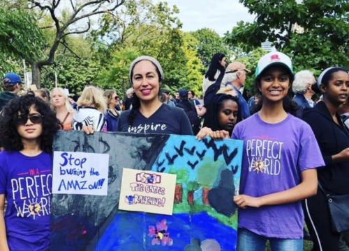 Two multi-ethnic teens holding a sign at a protest with their female teacher - empowering youth leadership in the community.