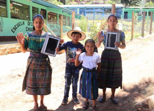 young students in Guatemala wave and hold up tablets that were donated to help their schooling