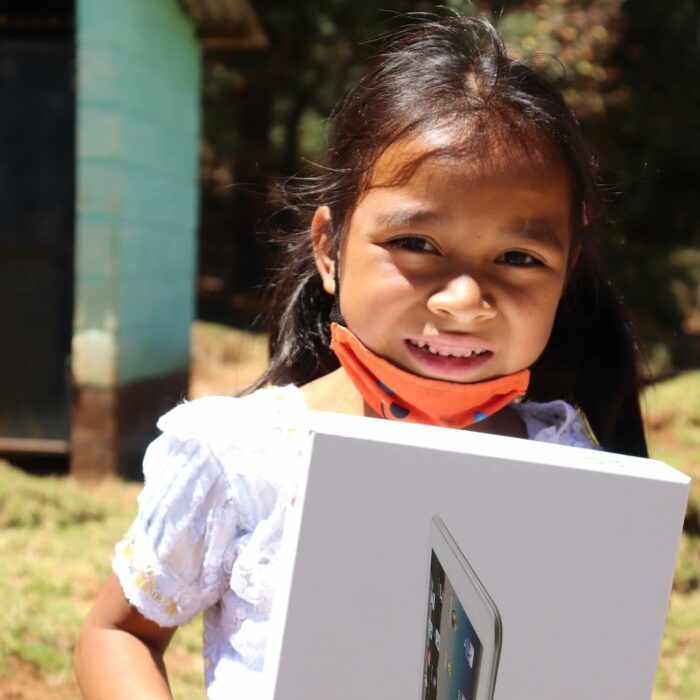 a young girl with a mask on smiles and hold a box with a new tablet that will help her education