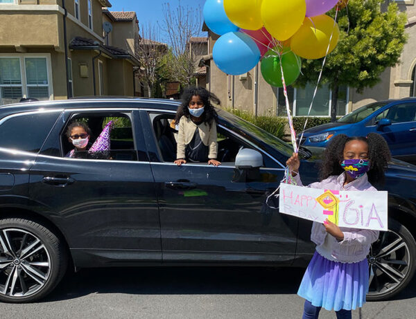 a group of young girls with masks on have balloons and signs for their friends birthday during the Covid pandemic when they weren't allowed to play with each other to cheer up their friend