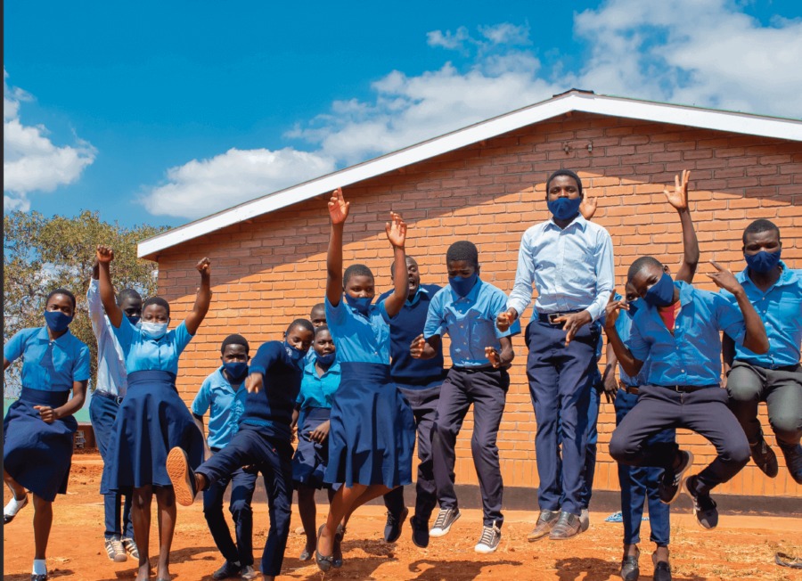 a group of Mbongozi Students jumping in the air in celebration of their new school standing in front of one of the new buildings