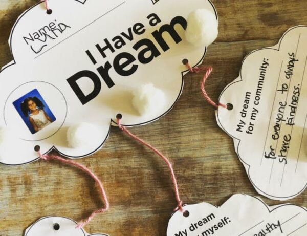 art projects of cut out clouds tied together with yarn lie on a table and say "I have a dream" on the front, and dream the children wrote on the back