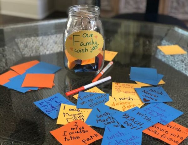 a table with a jar on it that says "Our Family Wish Jar" and several post it notes in different colors and hand written suggestions on them