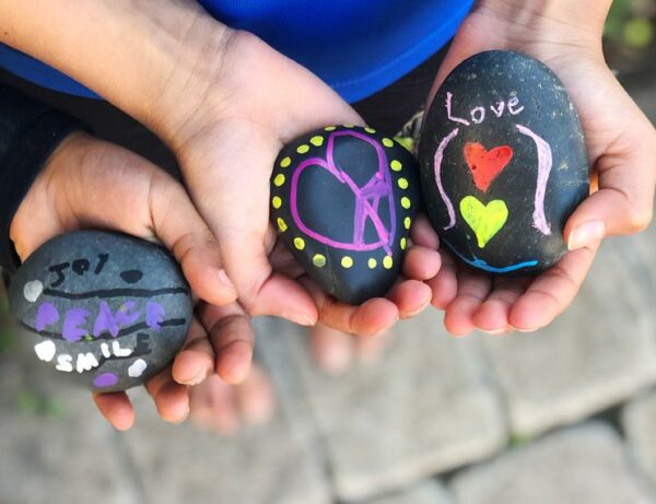 children hands hold black river rocks that were painted in bright colors with designs and the word love on them